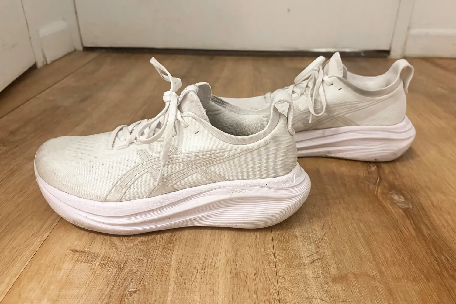 Pair of Asics Gel Nimbus 27 shoes on a wooden floor