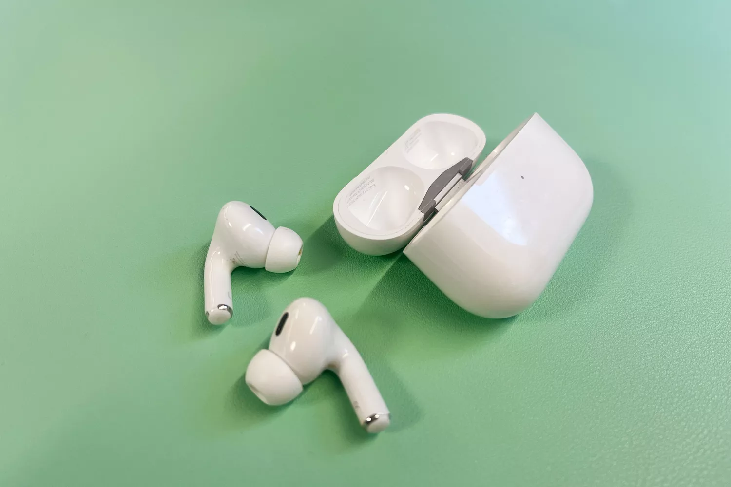 Apple AirPods Pro (2nd Generation) earbuds and charging case on a green surface