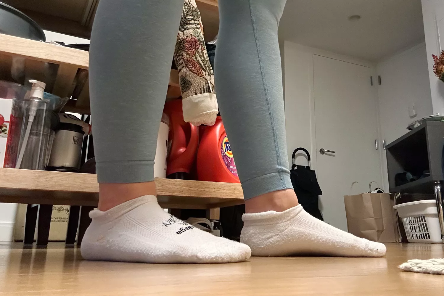 Feet wearing a white pair of Balega Hidden Comfort No-Show Running Socks on wood flooring