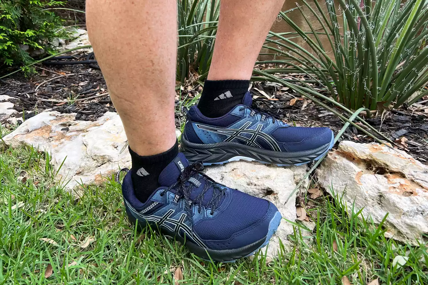 Feet wearing Asics Gel Venture 9 Shoes on rocks and grass