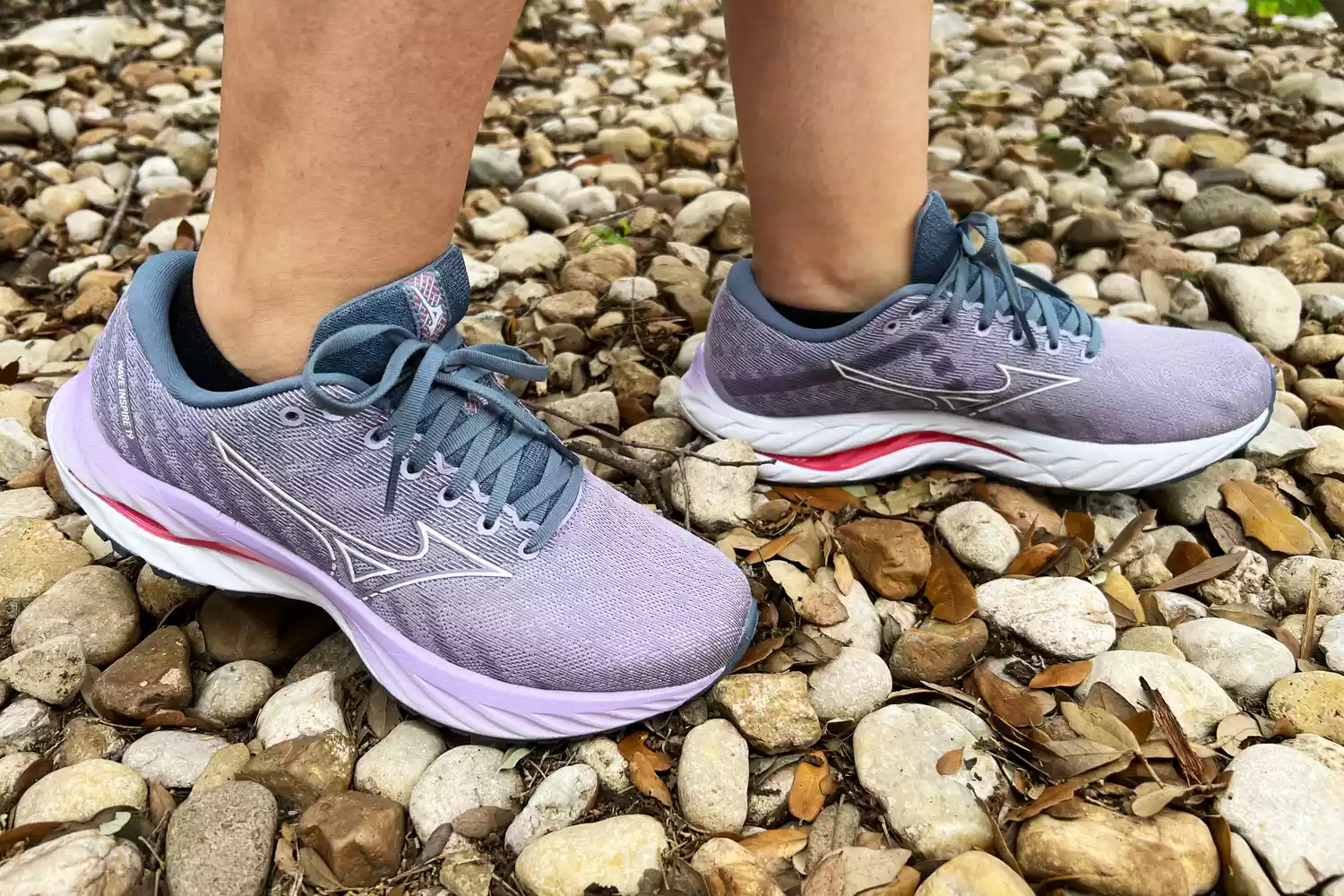 Feet wearing the Mizuno Women's Wave Inspire 19 Running Shoes while walking on pebbled path 
